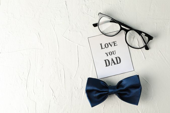 Inscription love you DAD, blue bow tie and glasses on plain background, space for text and top view