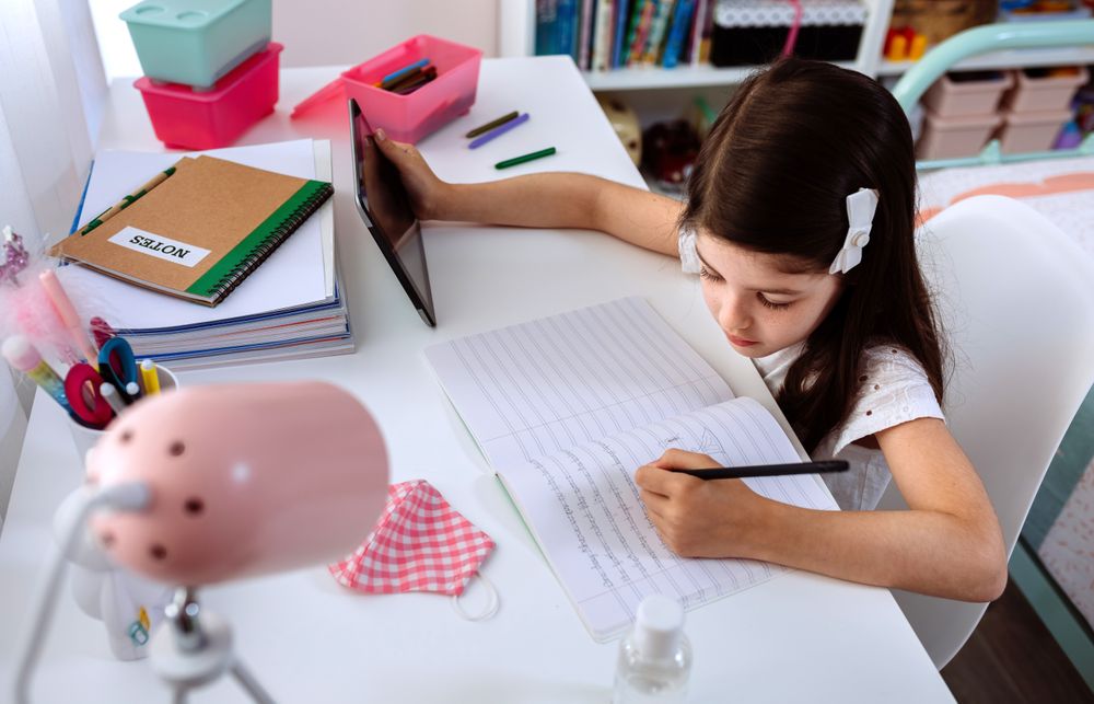 Girl studying at home with tablet and mask on table