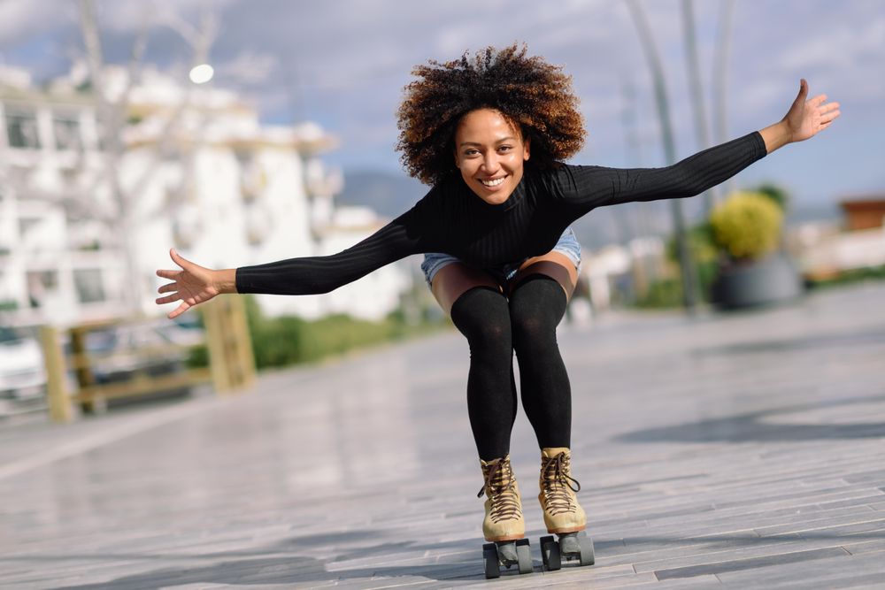 Black female with afro and arms spread roller skating outside