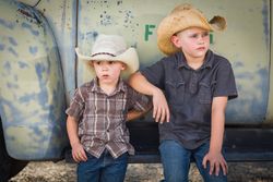 Two Young Boys Wearing Cowboy Hats Leaning Against an Antique Truck in a Rustic Setting
