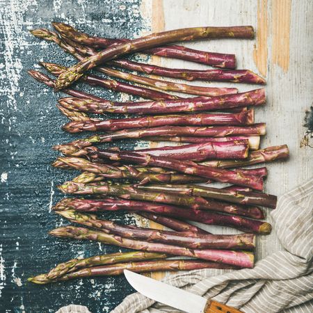 Scattered pieces of washed purple asparagus, on painted wood, square crop