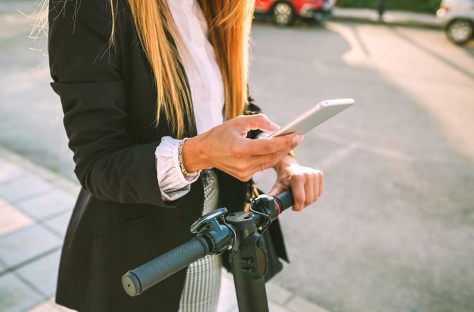 Unrecognizable businesswoman with e-scooter looking at cellphone