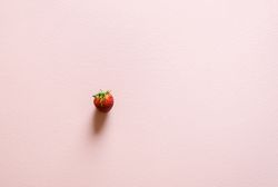Single organic strawberry on a pink table