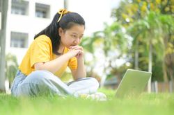 Woman sitting on the lawn looking at laptop, work from home.