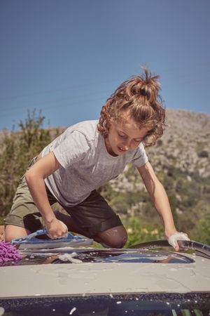 Little boy washing car in countryside