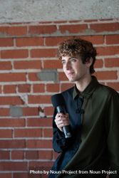 Nonbinary person holding microphone in front of brick wall 5nBMZ5