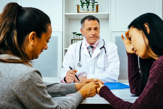 Concerned doctor sharing news with two sad patients in medical office