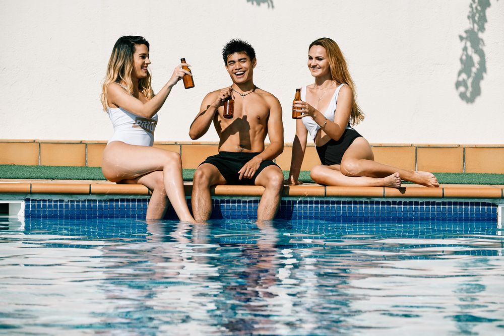 two young women and an asiatic man drinking beer by the pool