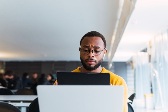 Man with earbuds using tablet and laptop at table