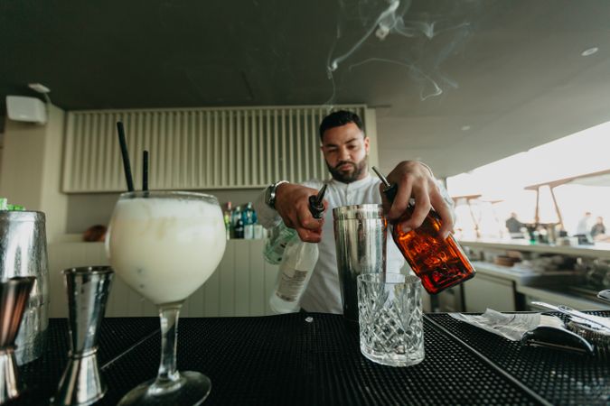 Barman pouring cocktail and alcoholic drinks to shaker in a bar.