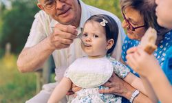 Older man feeding baby girl with spoon sitting in a bench