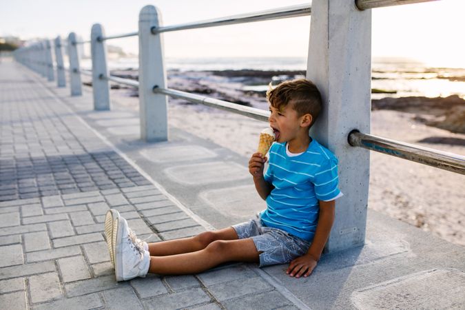 Boy eating an ice cream leaning on railing on the pier
