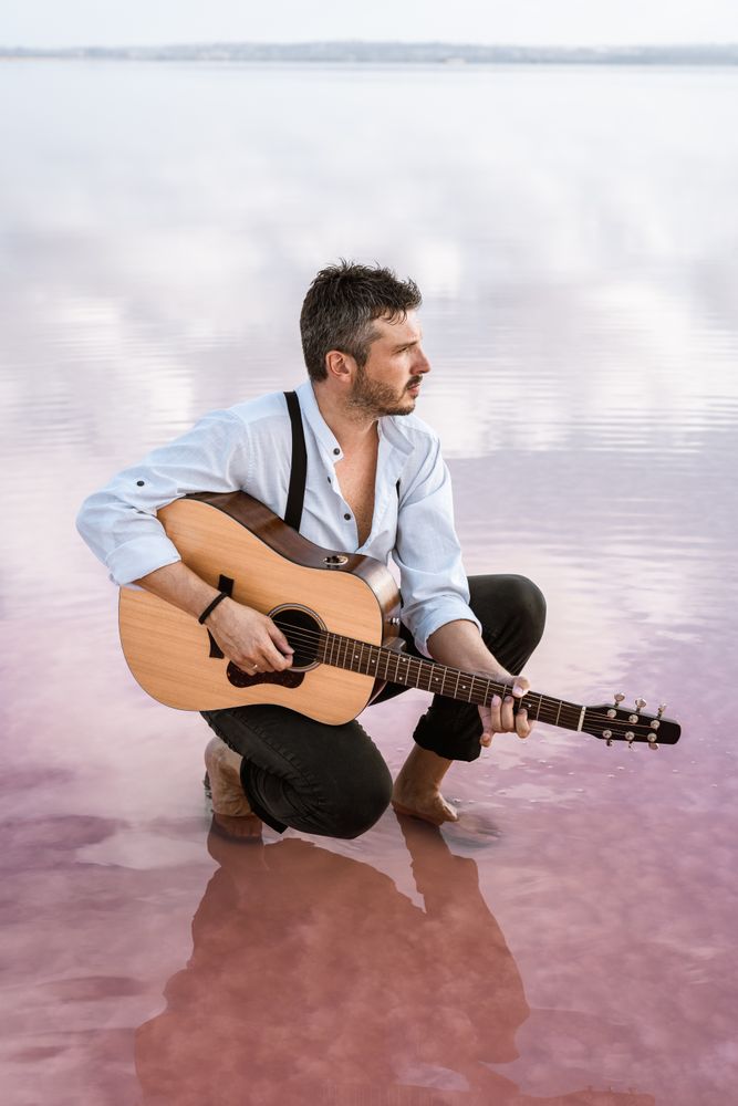 Musician with guitar on pink sandy water