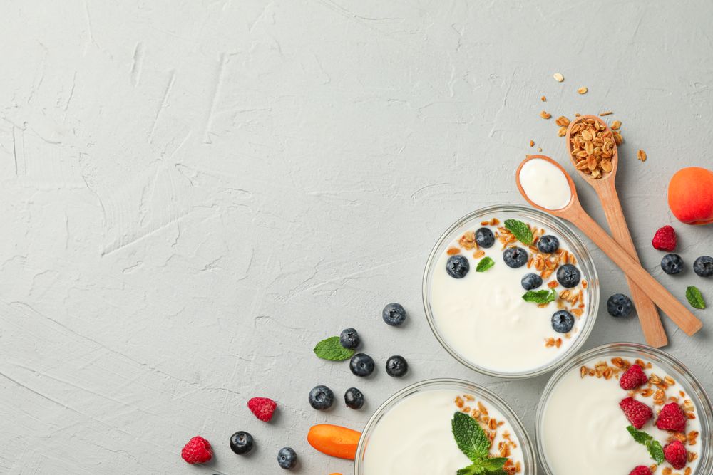 Flat lay composition with yogurt desserts and fruits on grey cement background