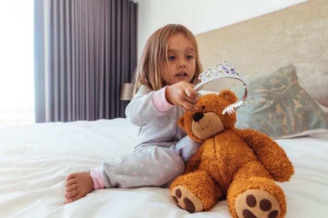 Little girl putting a crown on her teddy bear
