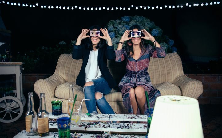 Funny young women holding smartphones showing male eyes