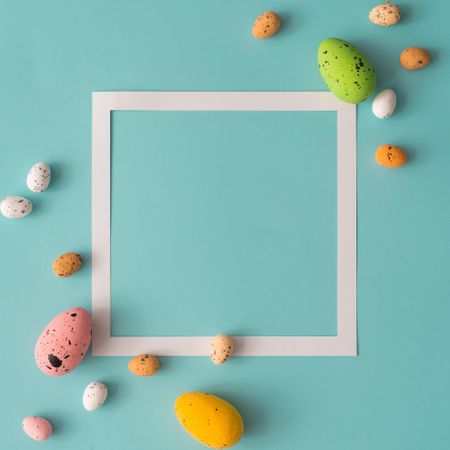 Easter composition made with colorful eggs on bright blue background with paper square outline