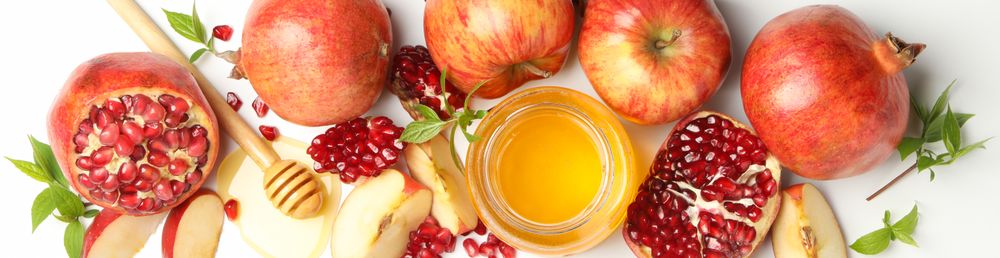 Wide shot of glass honey pot with pomegranate, and an apple quarters