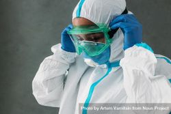 Side view of Black female medical worker putting on PPE goggles 47WjP4