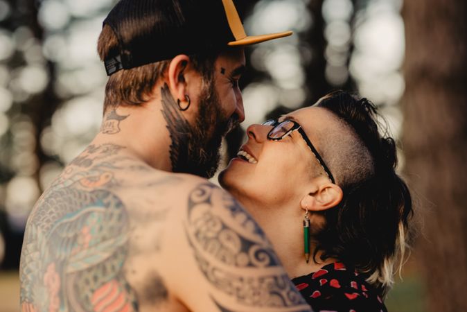Young guy in tattoos hugging woman in forest