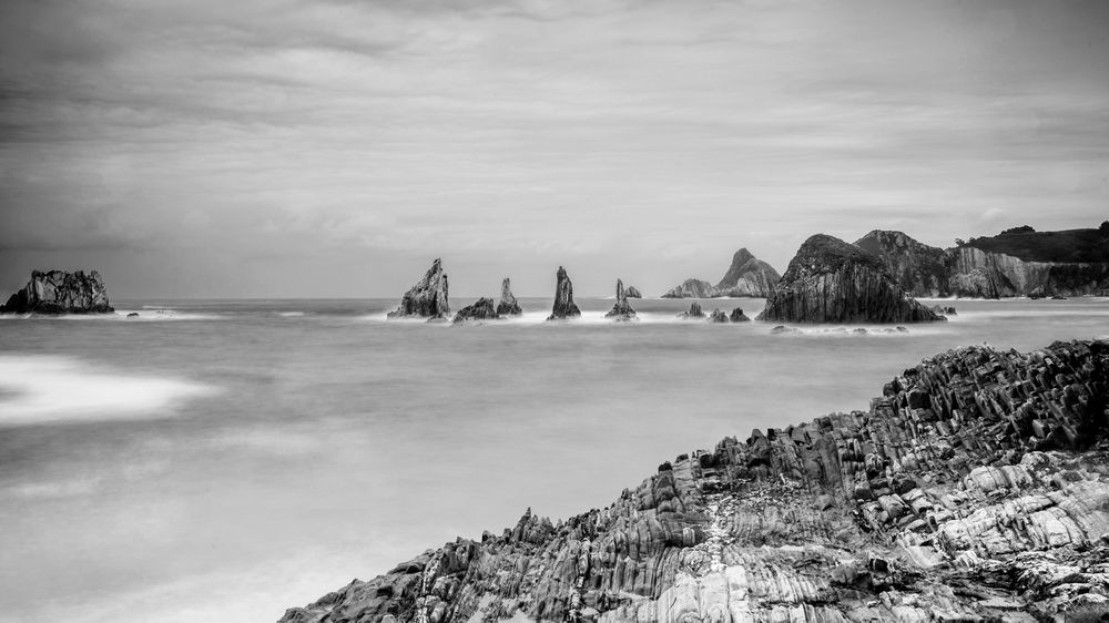 Rocky peaks protrude from water in cloudy day