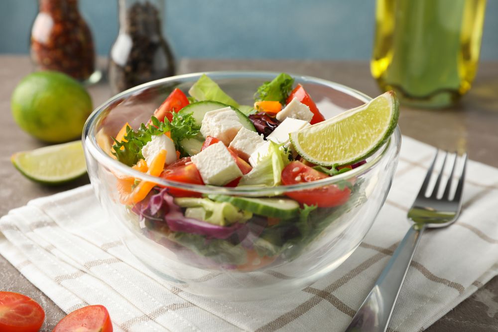Glass bowl with salad, towel and spices on grey background, space for text