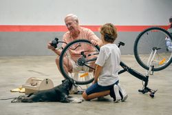 Smiling grandfather inflating bicycle wheel with grandson and dog