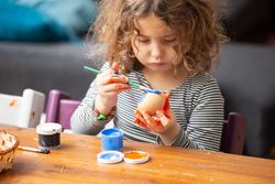 Toddler girl painting egg at table