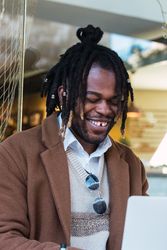 Happy Black man browsing on laptop on restaurant terrace