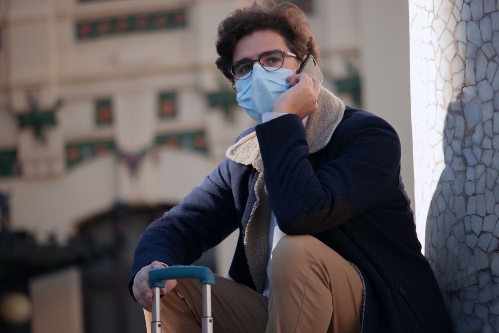 Man wearing facemask talking on phone sitting on floor