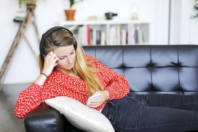 Calm woman listening to music wearing headphones using a smartphone relaxing at home