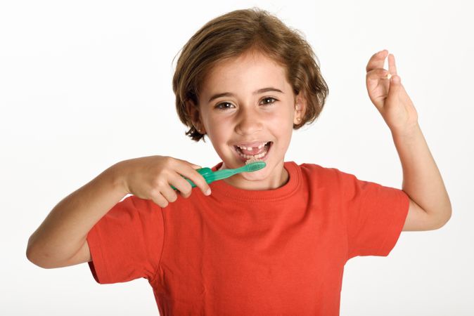 Smiling child brushing her teeth while holding a lost tooth
