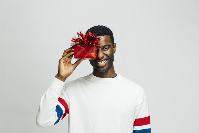 Excited Black man hiding one eye behind a present wrapped in red