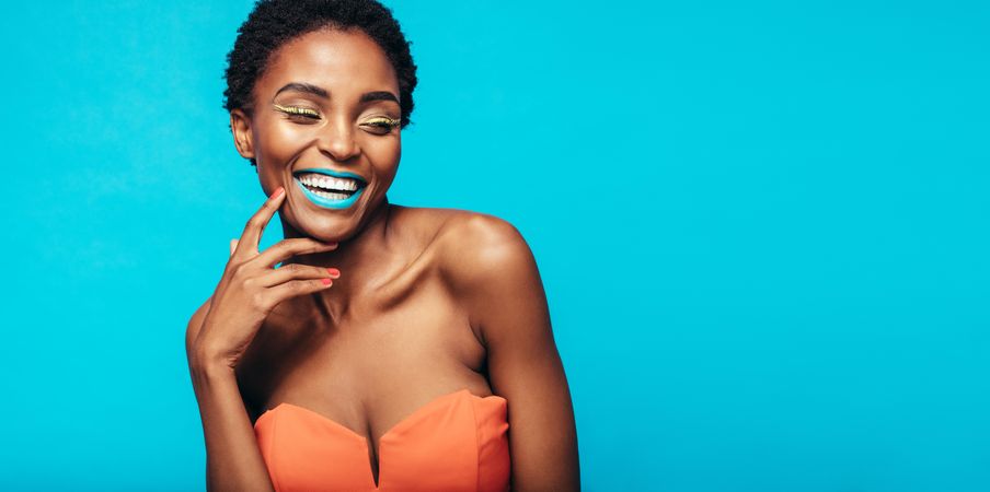 Woman with vivid makeup smiling against blue background