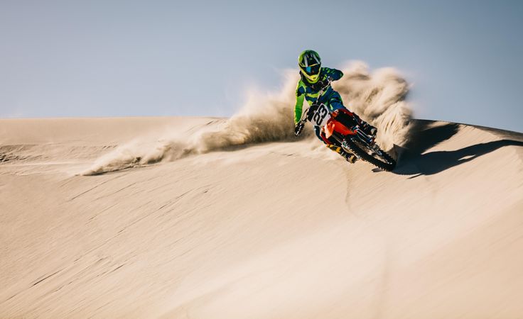Enduro rider in action accelerating the motorbike after the corner on sand dune