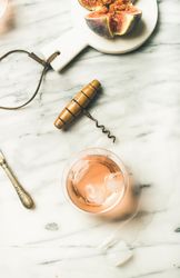 Rose wine in glass on marble table with quartered fig, knife and corkscrew