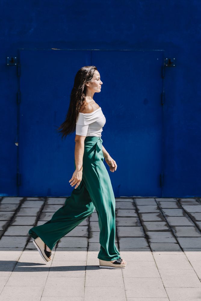 Young happy trendy woman walking in city against blue door