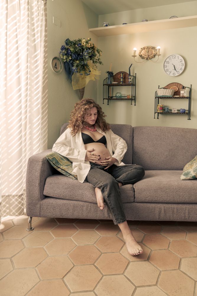 Pregnant woman relaxing at home on the sofa touching her belly.
