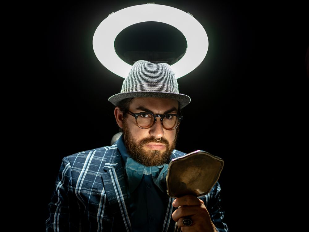 Fashion man in hat holding hand mirror and looking at camera