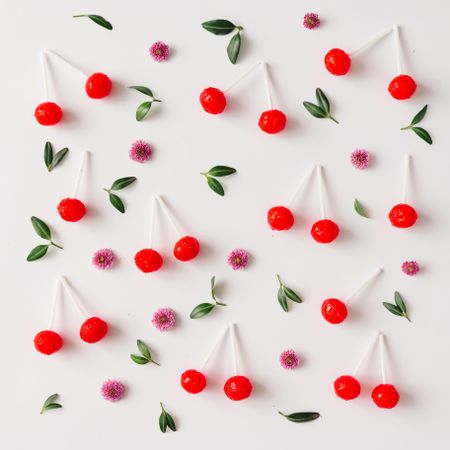 Colorful pattern made of red cherry lollipops, leaves, and flowers
