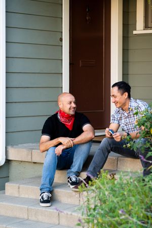Angled view of two men sitting on steps in front of a house laughing and having fun