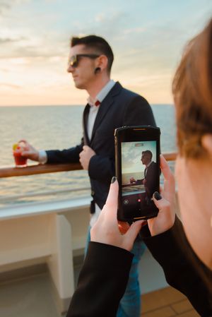 Woman taking photo of man on deck of ship at sea
