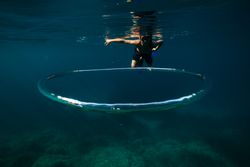 Young male tourist diving in blue ocean near bubble ring in sunlight