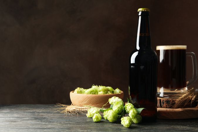 Beer, hop and wheat on wooden table against brown background