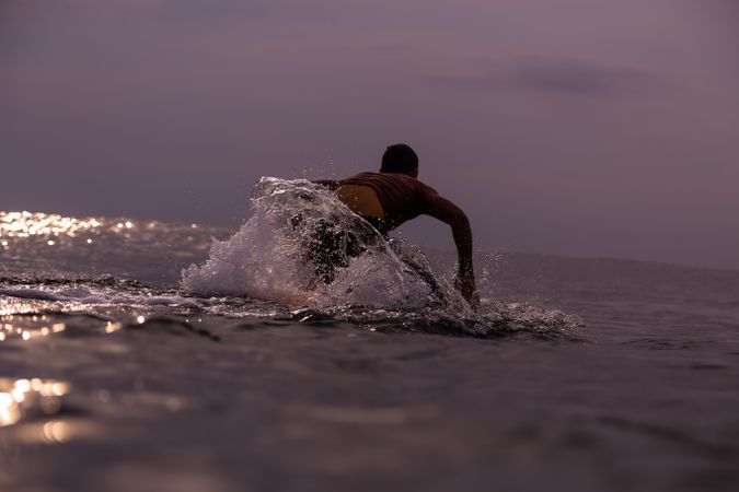 Man on surf board floating on water and cloudy sky