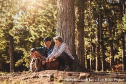 Portrait of mature couple sitting together under a tree with backpacks and compass 5qPyp0