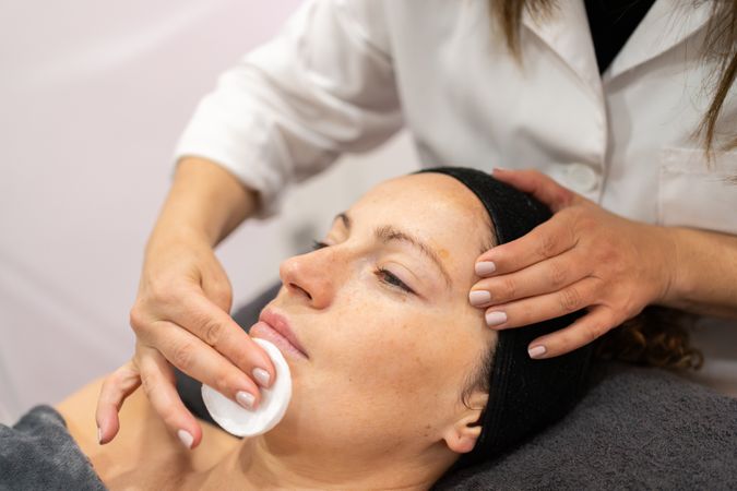 Beautician cleansing face of female customer in beauty salon