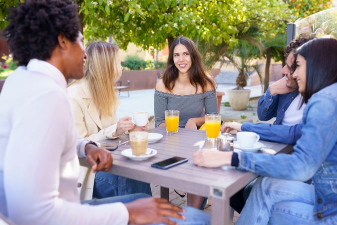 Multi-ethnic friends smiling and talking outside with drinks
