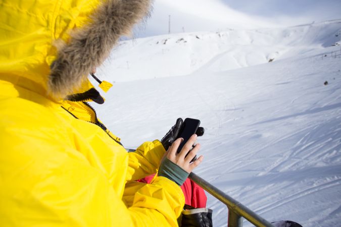 Man in yellow hooded parka checking cell phone on ski lift