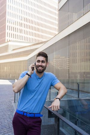 Man leaning on glass railing outside having conversation on mobile phone